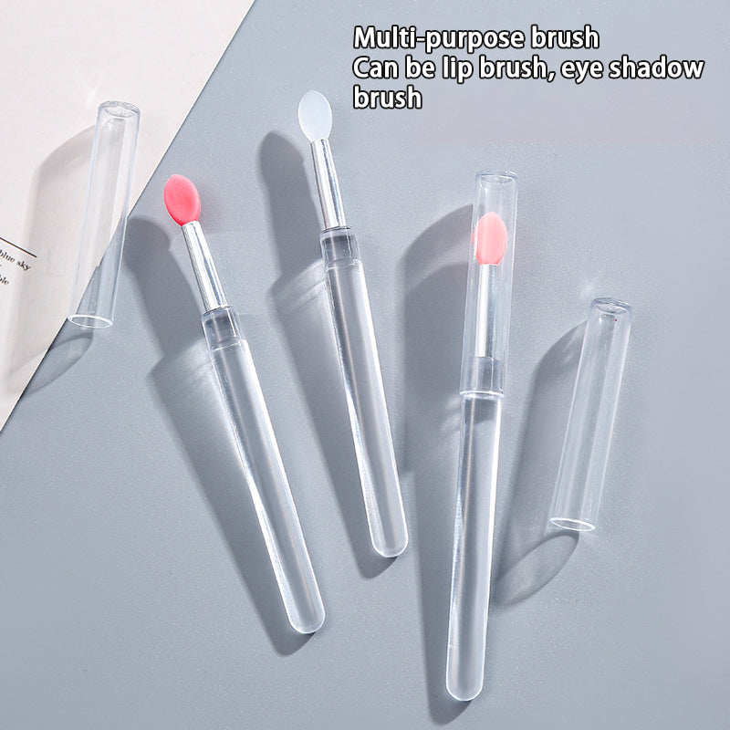 Multi-purpose lip and eye shadow brush with clear handle and pink bristle tip on a gray background.