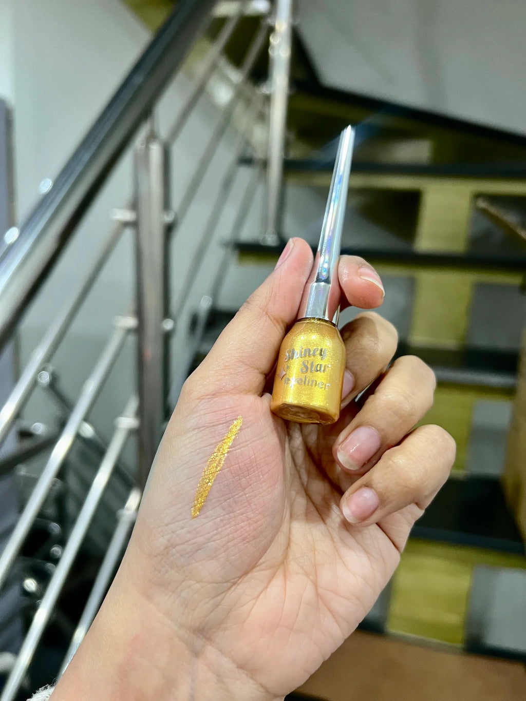Hand holding a small bottle with a brush, with a blurred staircase in the background