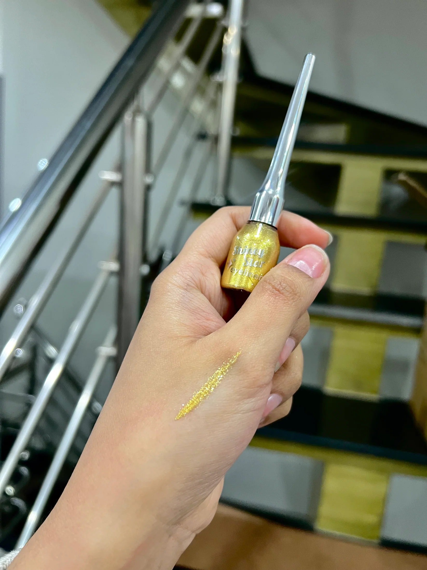 Hand holding a small bottle with a dropper against a blurred staircase background