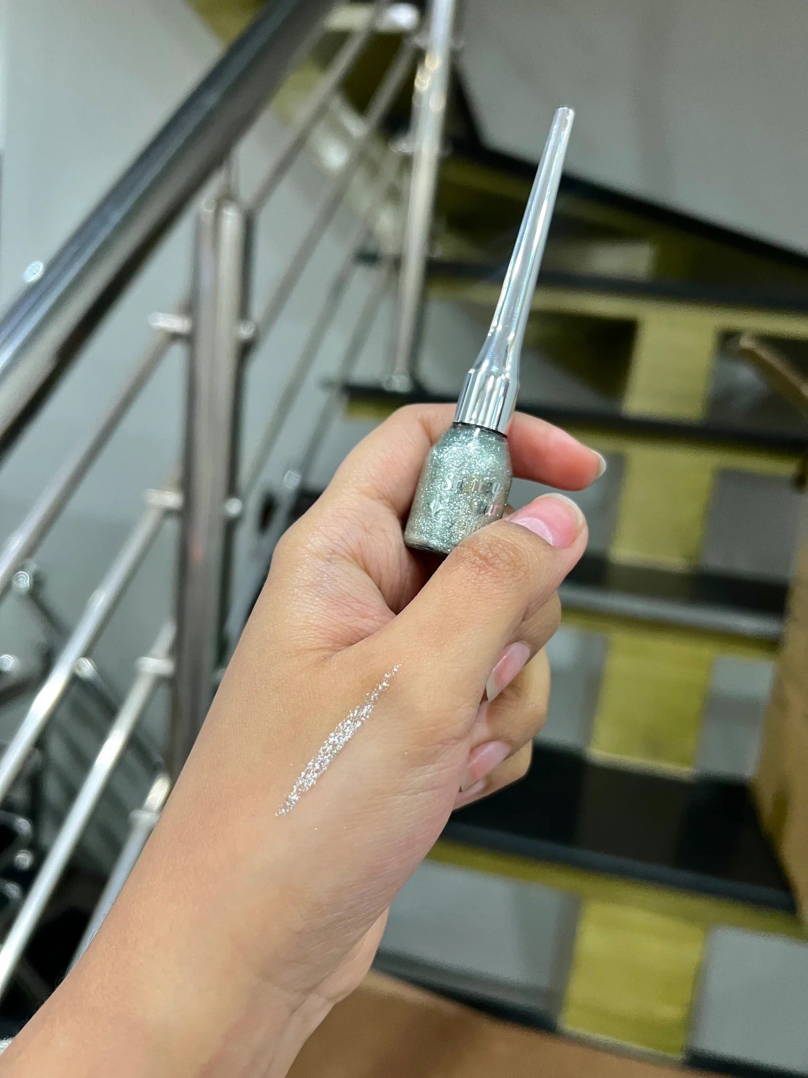 Hand holding a small bottle of glittery liquid with a staircase in the background