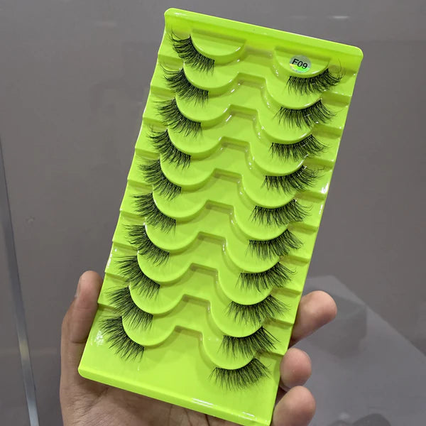 Set of false eyelashes on a green tray held by a hand against a gray background