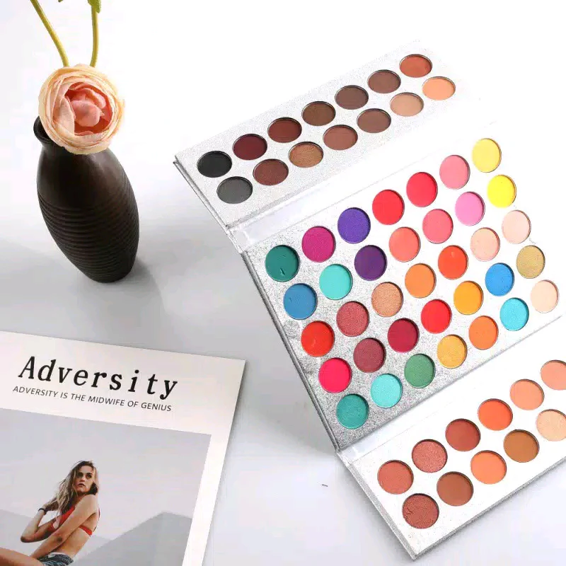 Makeup palettes with a vase and book on a white surface