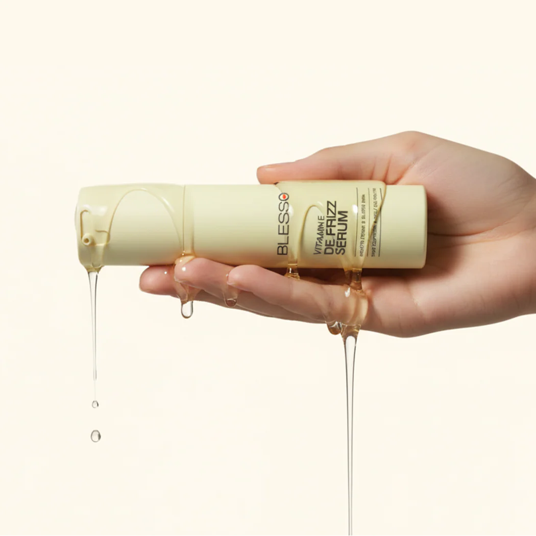 Hand holding a bottle of Belvese Vitamin E Hair Serum with visible serum dripping.