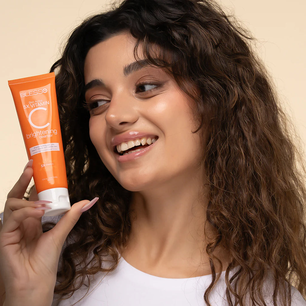 Woman holding an orange skincare Blesso product with a beige background