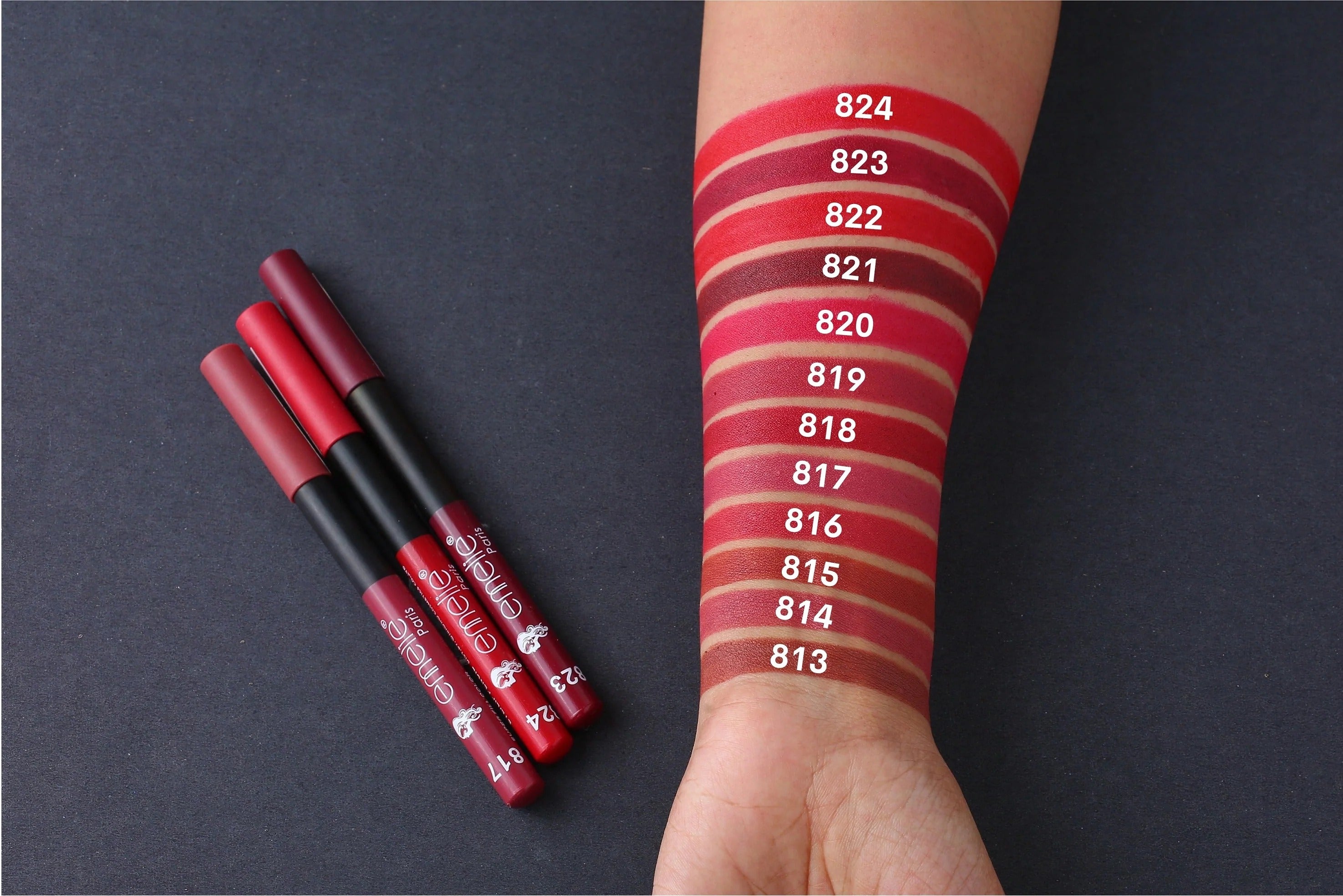 Three lipsticks with their corresponding shades on a swatch on a dark background