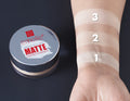 Emelie Matte Loose Powder container with swatches on a wrist against a dark background