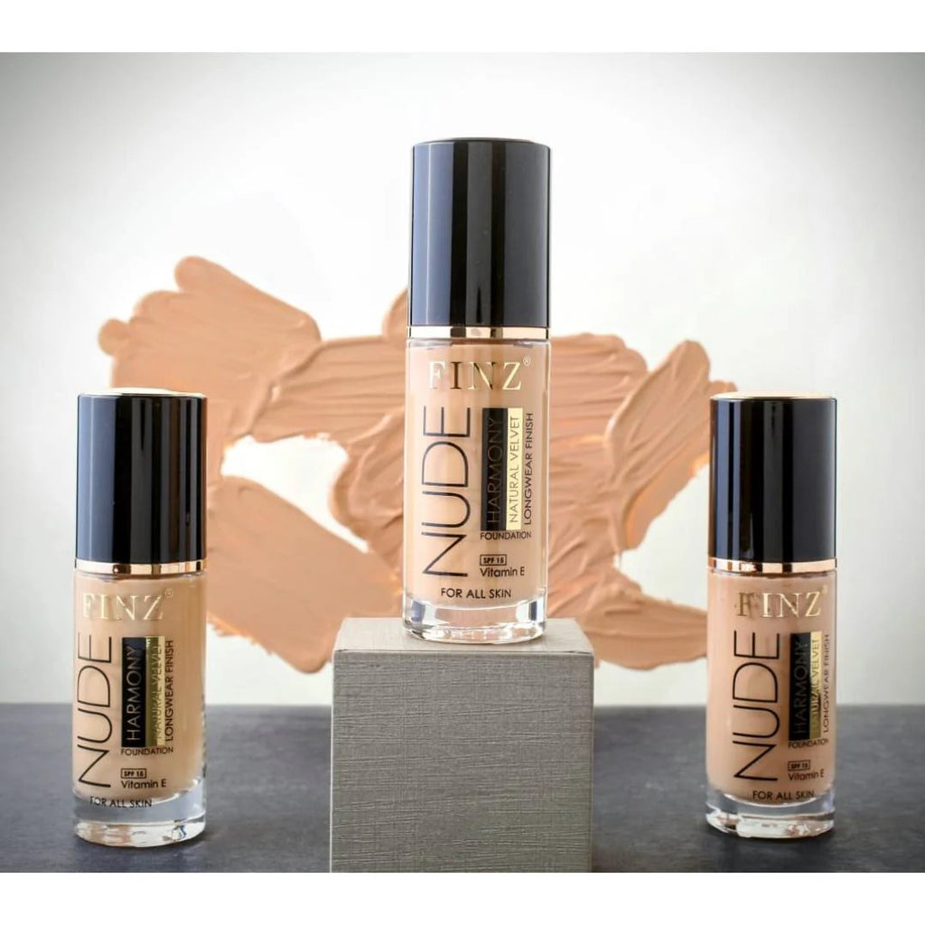 Three bottles of FINZ Nude foundation on a gray surface with a beige swatch in the background.