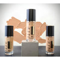 Three bottles of FINZ Nude foundation on a gray surface with a beige swatch in the background.