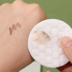 Cotton pad with makeup residue on a hand with swatches of makeup.