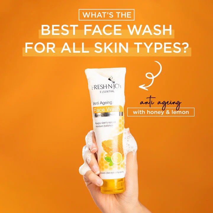 Hand holding a tube of Fresh n Joy Face Wash - Anti Ageing With Honey & Lemon against an orange background with text about skin types.