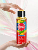 Hand holding a Golden Pearl Seduce Body Spray bottle with colorful design against a soft, multicolored background