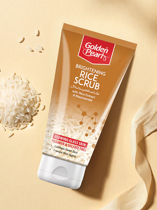 Golden Pearl Brightening Rice Scrub tube on a beige background with rice grains.