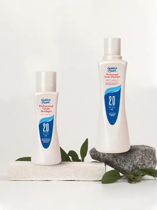 Two bottles of Golden Pearl Cream Developer products on a white background with green leaves.