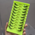 Set of false eyelashes on a green tray held by a hand against a gray background