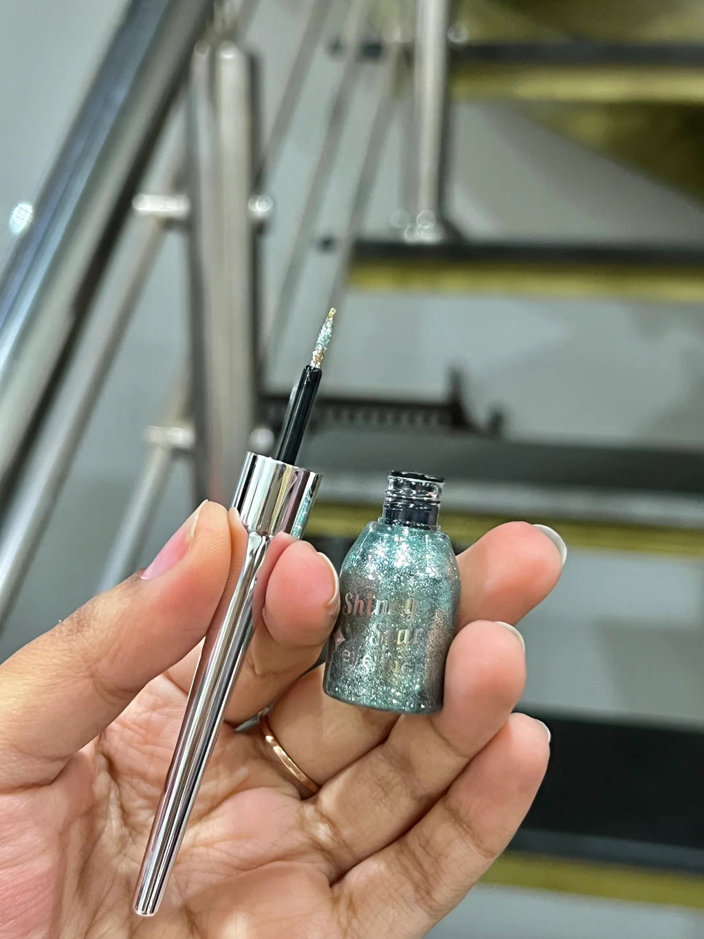 Small silver pen and glittery bottle held in a hand with a blurred background
