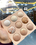 Makeup palette with gold and bronze shades held by a hand in an indoor setting.