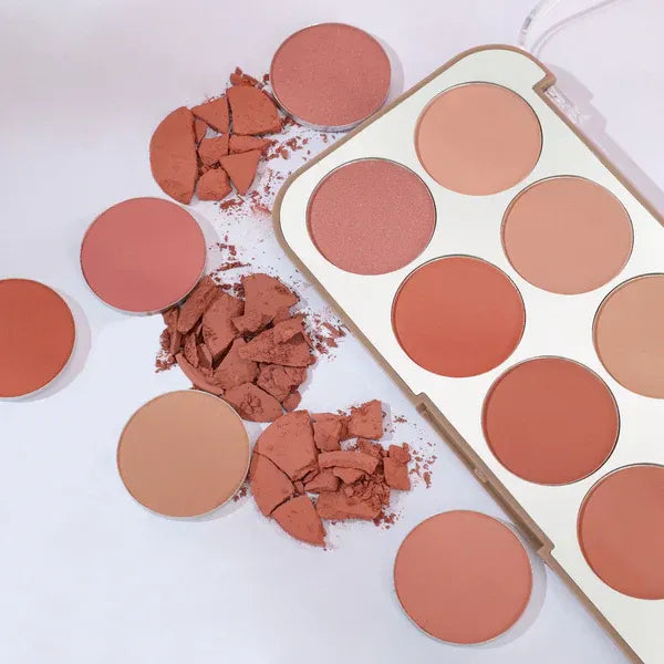 Makeup blush palette with round compartments and scattered pressed powder on a white background