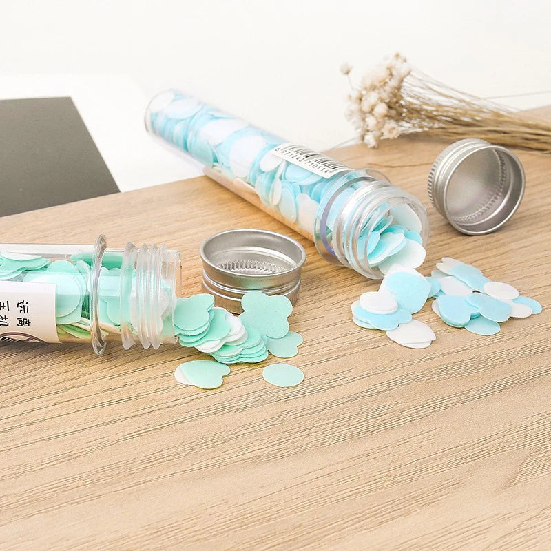 Mint green confetti in an open cylindrical container on a wooden surface.