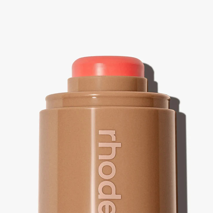 Cosmetic stick with coral-colored cap on a white background, featuring the brand 'rhode'.