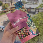 Hand holding a 'Beauty World' makeup kit with peacock design against an outdoor background